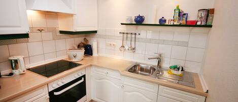 A compact kitchen with white cabinets, a stove, an oven, a sink, and a countertop.