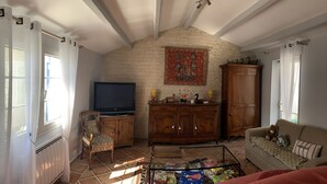 Una sala de estar con televisor, muebles de madera, un tapete estampado y una pared de ladrillo.