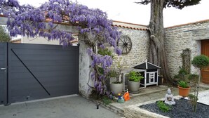 Un edificio de piedra con una verja negra, una pequeña construcción blanca y enredaderas moradas en flor.