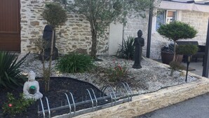 Edificio de piedra con jardín que presenta una estatua de Buda, un árbol en maceta y diversas plantas.