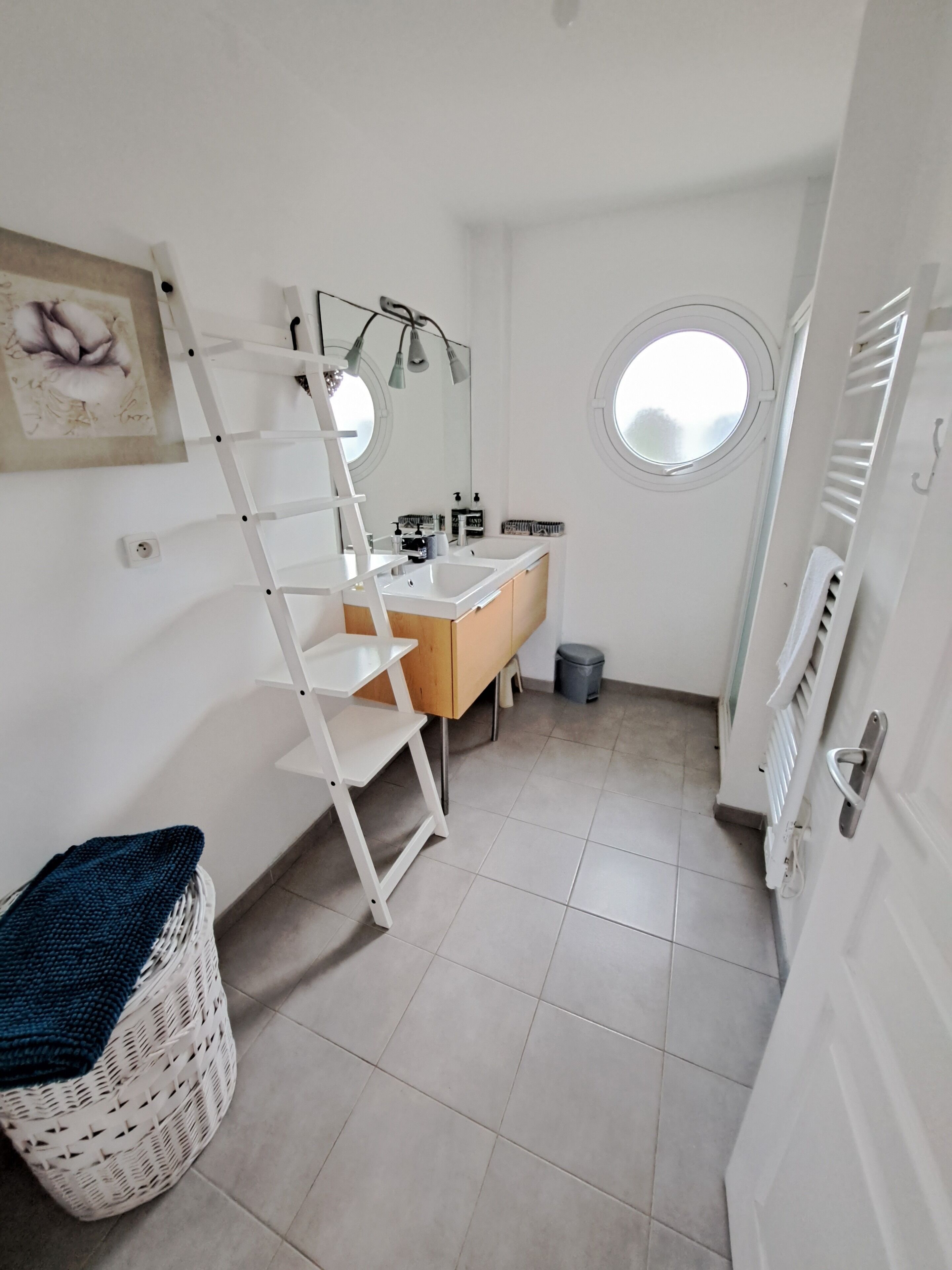 A small, bright bathroom with a white vanity, a mirror, and a window.