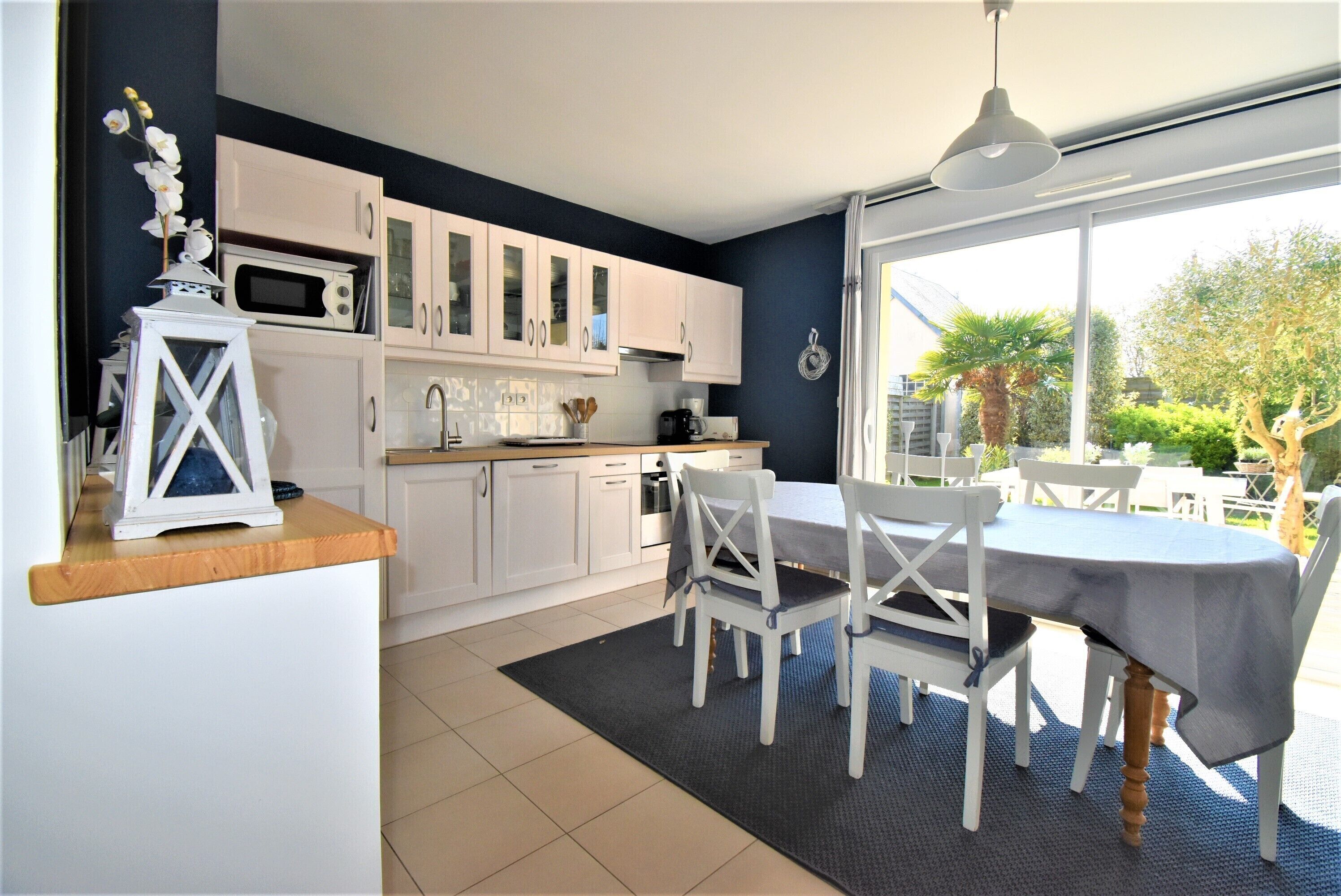 Une cuisine moderne avec des meubles blancs, une table à manger avec des chaises et une vue sur l’extérieur.