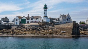 Uma vila costeira com um farol imponente, muros de pedra e edifícios tradicionais.