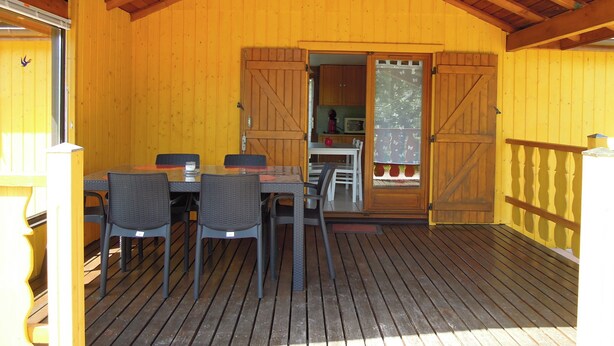 Ett trädäck med ett bord och stolar, ett träpanelat tak och utsikt över ett köksområde genom en dörr.