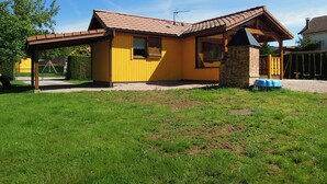 Ett gult hus med ett tak täckt av tegelpannor, en inglasad veranda och en skorsten av tegel.