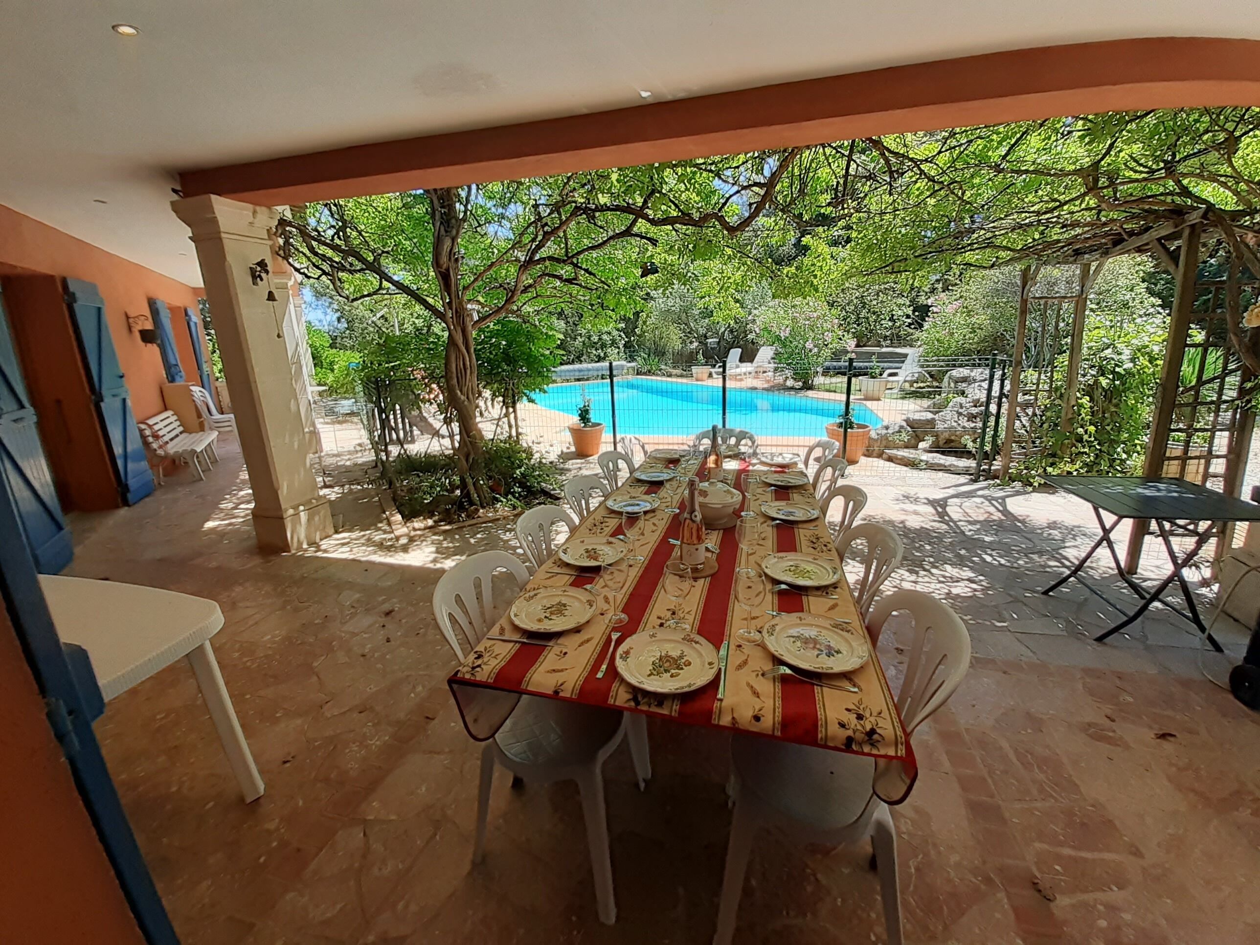 A covered outdoor dining area with a pool in the background.