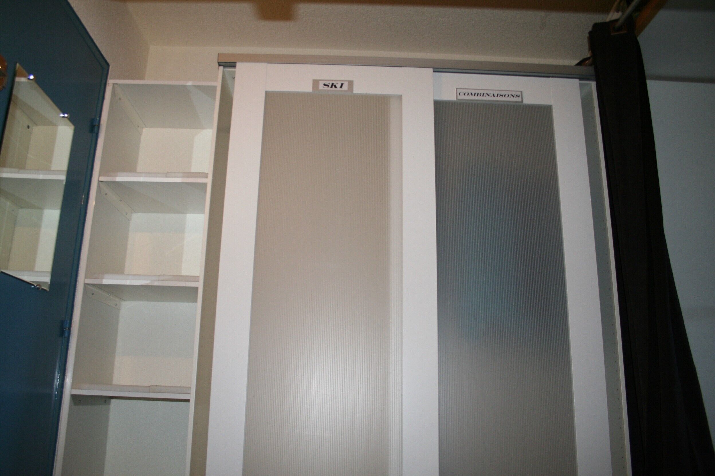 Une pièce avec une armoire blanche, un mur bleu et une porte avec un rideau noir.