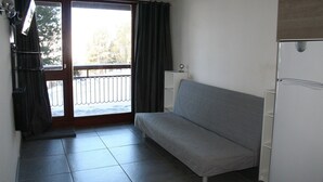 A small, sparsely furnished room with a sliding glass door leading to a balcony, a white refrigerator, and a grey sofa. - Apartment with balcony at the foot of the slopes - Arc 2000 (Bourg-Saint-Maurice)