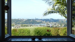 Une vue depuis une fenêtre donnant sur une ville avec des maisons, de la verdure et une tour qui se dresse au loin.