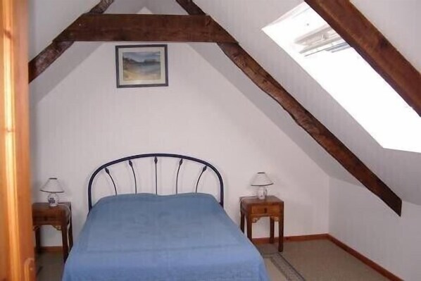 A bedroom with a sloped ceiling, a bed with a blue bedspread, two bedside tables with lamps, and a framed picture on the wall.
