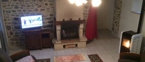 A living room with a stone wall, a fireplace, a television, and a modern heater.