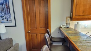 A compact kitchen with a wooden door, a bar area with stools, a framed picture on the wall, and a lamp on a table. - Quiet 
2 Bedroom/2 Bath Condo Sleeps 8 (Solitude)