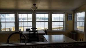 Une pièce dotée de grandes fenêtres donnant sur un lac, une table à manger avec des chaises et un ventilateur de plafond.