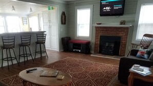 Un salon doté d’une cheminée, d’un téléviseur fixé au mur et d’un coin bar avec des tabourets.