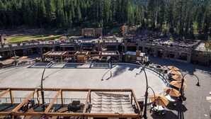 A spacious outdoor area with seating and a stage, surrounded by buildings and a forested backdrop. - Vacation condo in Northstar village. Perfect location overlooking the mountain. (Truckee)