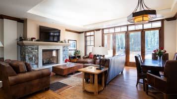 A spacious living room with a fireplace, leather sofas, a dining table, and large windows.