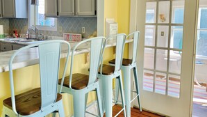 Une cuisine avec un plan de travail en marbre, un évier et une enseigne indiquant « Paradise ». On y trouve des chaises bleu clair et une affiche présentant le « menu à emporter ».