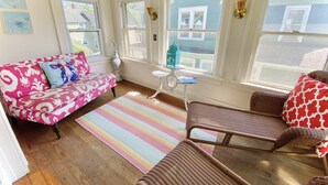 Une pièce chaleureuse avec un canapé rose à motifs, un fauteuil en osier, un tapis rayé et une petite table sur laquelle est posée une lanterne bleue.