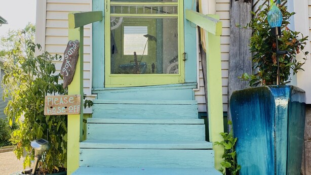 Une maison avec une porte d’entrée peinte en bleu, un paillasson sur lequel est écrit « Bonjour » et une pancarte indiquant « Veuillez fermer la porte ».