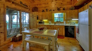 Une cuisine rustique aménagée dans une cabane en bois, avec une table à manger, des chaises, un réfrigérateur et un four à micro-ondes.