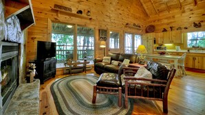 Un intérieur de chalet chaleureux avec une cheminée, des meubles en cuir et de grandes fenêtres.