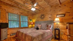 Une chambre dans une cabane en bois, équipée d’un lit, d’une télévision et d’un ventilateur de plafond.