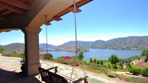 Une terrasse couverte avec une chaise suspendue, donnant sur un lac et des montagnes.