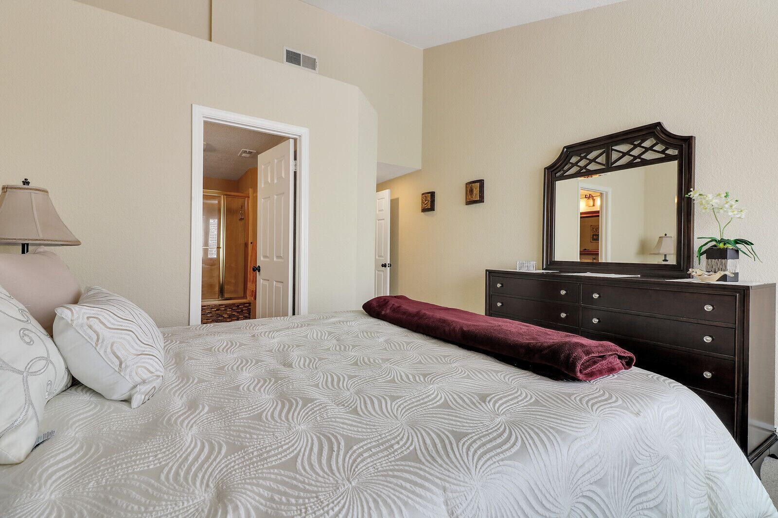 A bedroom with a bed, a dresser, a mirror, and a door leading to another room.