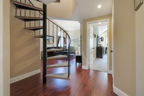Una escalera con un rascador para gatos, suelo de madera y una puerta que da a otra habitación.