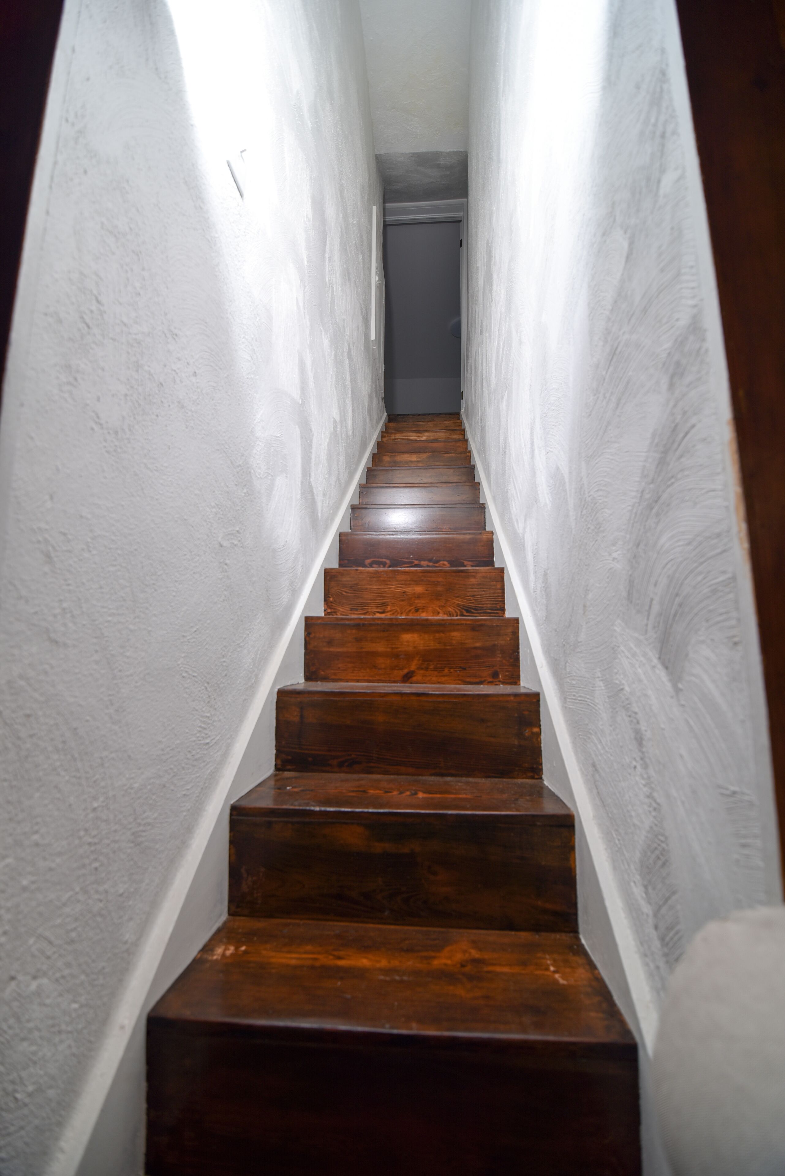 Una escalera de madera en un estrecho pasillo con paredes blancas.