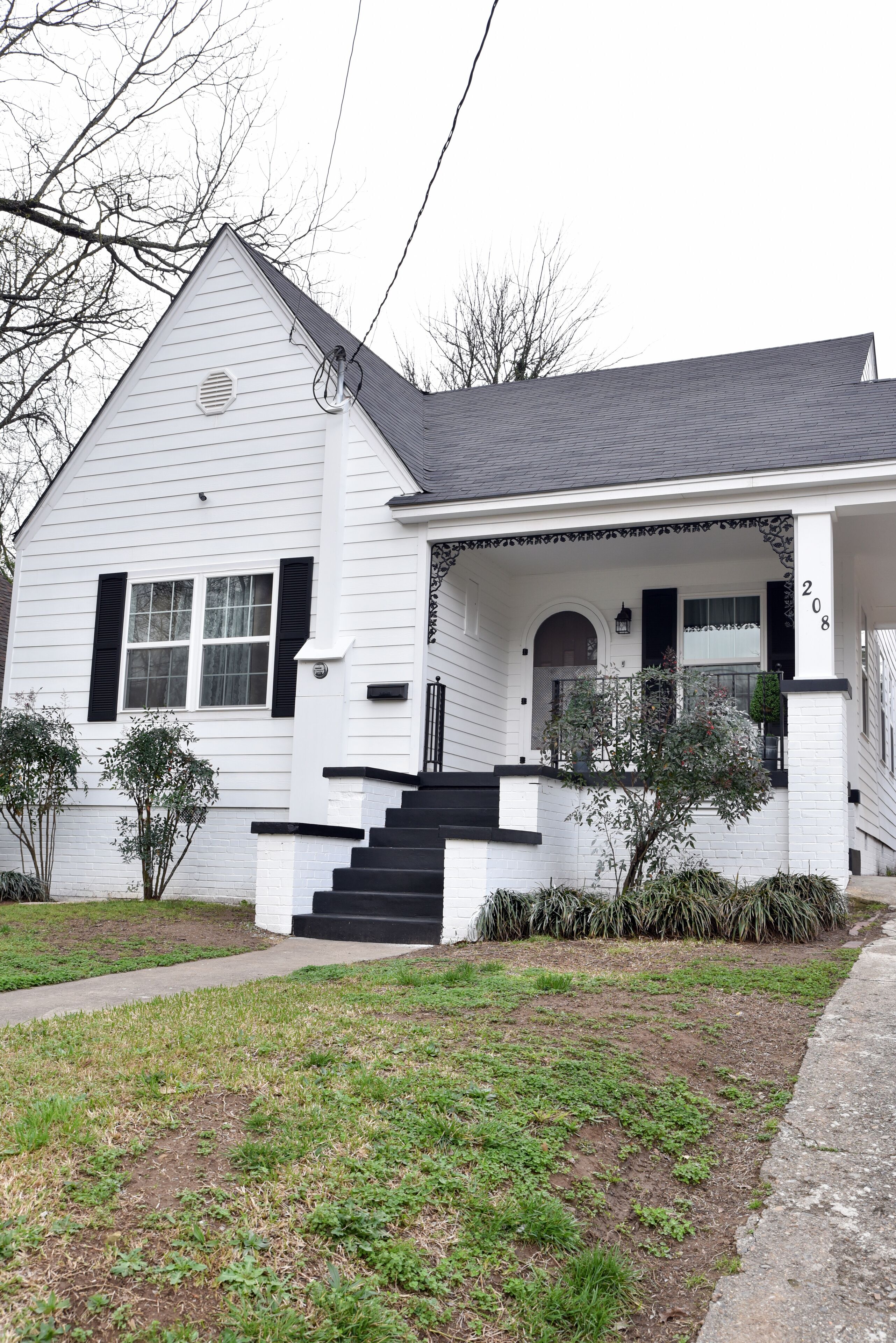 A white house with black shutters, a front porch, and a number '208' on the side.