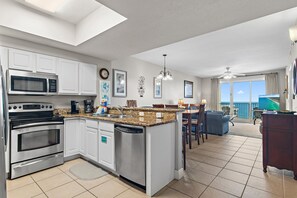 A modern kitchen with built-in appliances, a dining area with a view, and a living room with a balcony overlooking the sea.