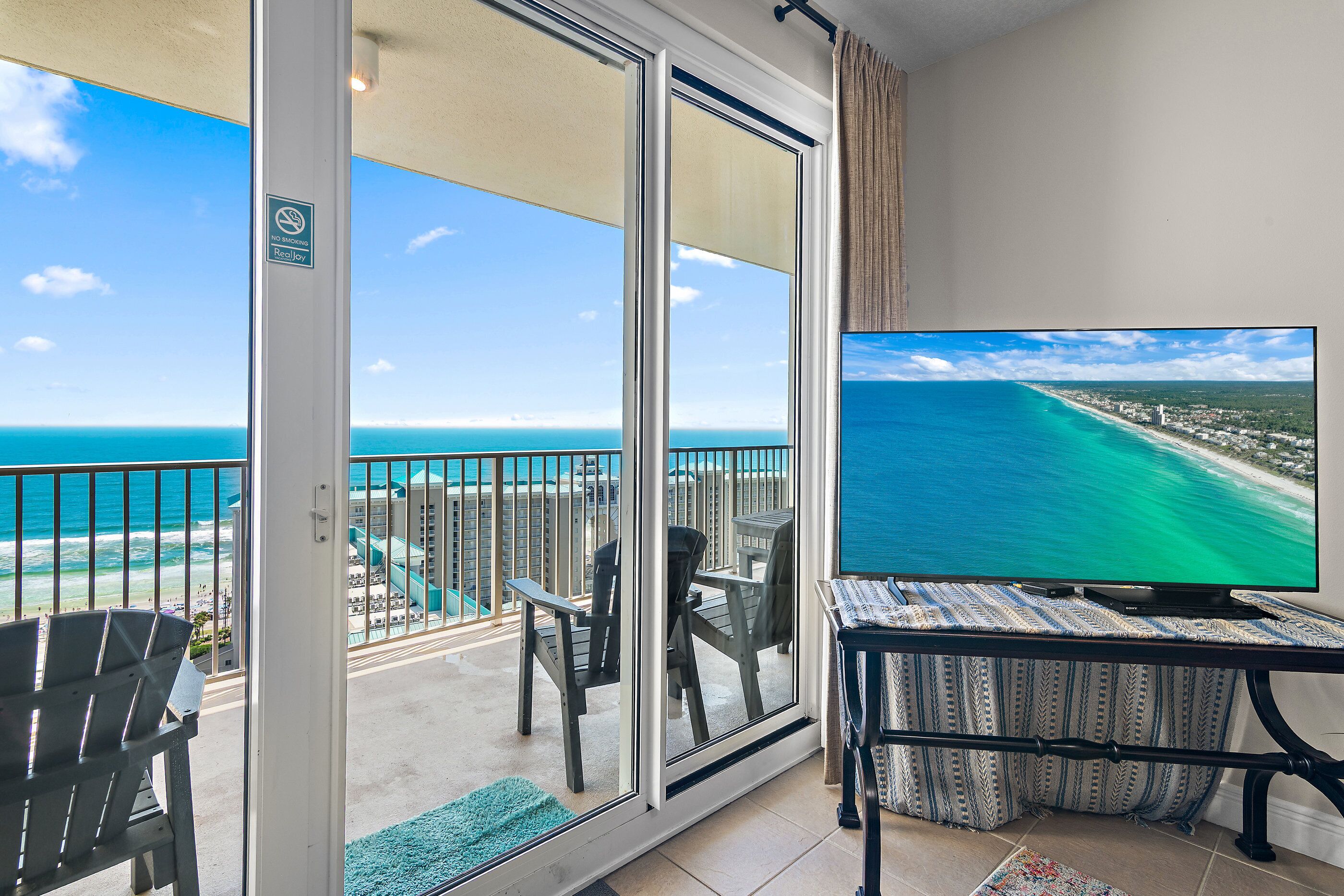 A balcony with a view of the ocean, a television, and outdoor furniture.