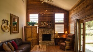 A cozy living room with a stone fireplace, leather furniture, and wooden walls.