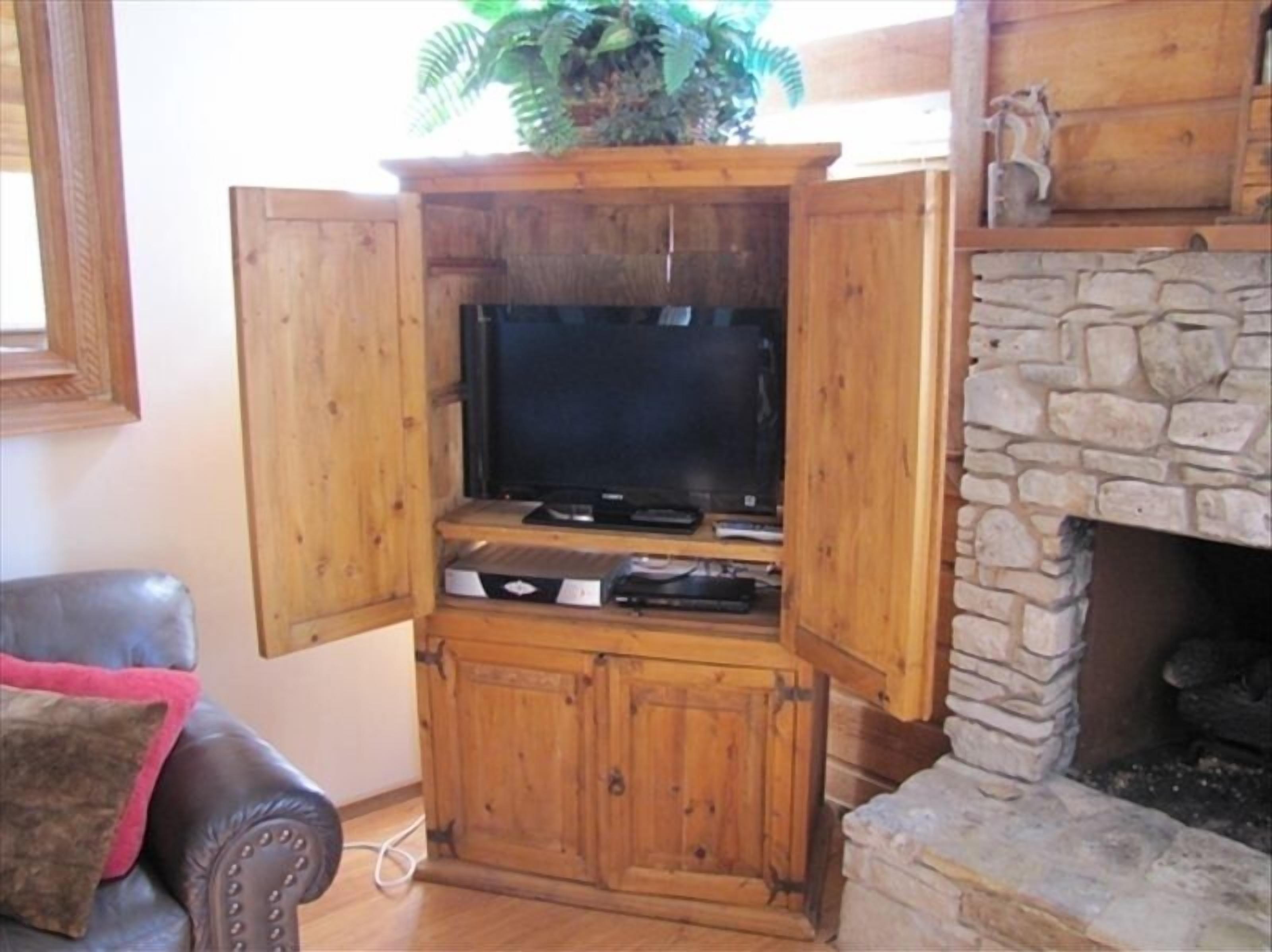 A wooden entertainment center with a television, DVD player, and gaming console.