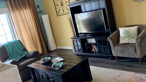 A living room with a sofa, a coffee table, a television, and a fireplace. - Mermaid Lookout Beachfront Condo (Galveston)