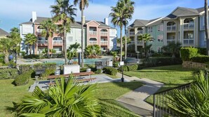 A resort with multiple-story buildings, a swimming pool, and palm trees. - Mermaid Lookout Beachfront Condo (Galveston)