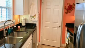 A kitchen with a double sink, a refrigerator, and a door with a decorative crab wall hanging. - Mermaid Lookout Beachfront Condo (Galveston)