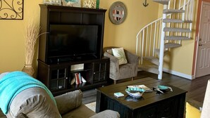 A living room with a fireplace, a television, and a staircase with a cat tree. - Mermaid Lookout Beachfront Condo (Galveston)