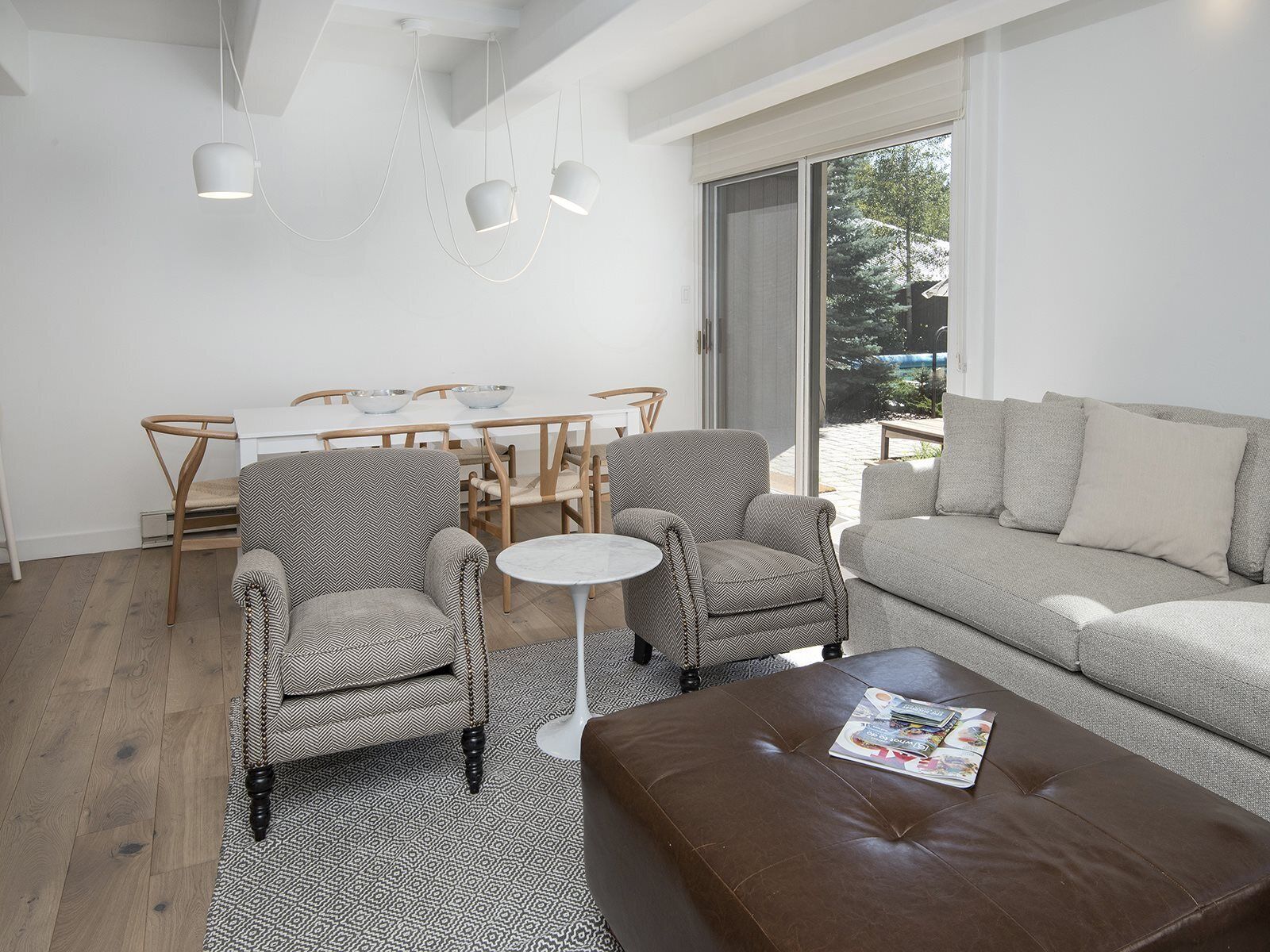 Un soggiorno moderno con un divano, due poltrone, un tavolino da caffè e un tavolo da pranzo con sedie. Una grande finestra offre vista sull'esterno.
