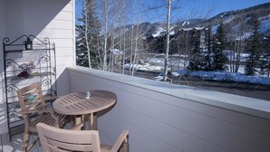 En balkong med ett runt bord och två stolar, med utsikt över ett snöklätt berglandskap.