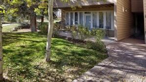 A building with a covered outdoor seating area, a paved walkway, and a grassy lawn with trees. - Sun Vail 14-e (Vail)