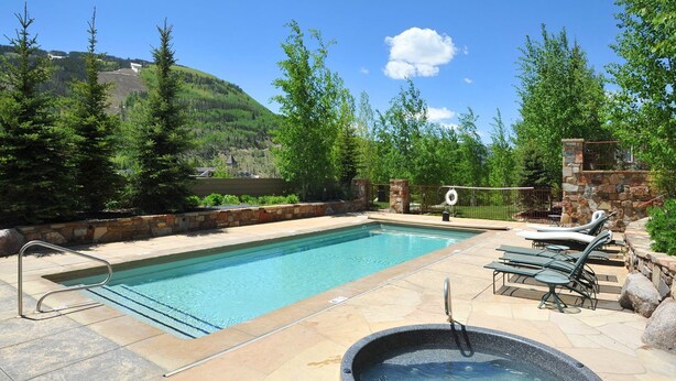 A rectangular swimming pool with a stone deck, surrounded by lounge chairs and a hot tub. - Sun Vail 14-e (Vail)