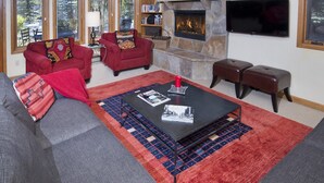 A cozy living room with a stone fireplace, red and grey sofas, a coffee table with magazines, and a television on the wall. - Sun Vail 14-e (Vail)
