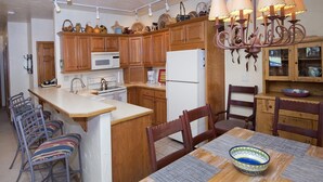 A kitchen with wooden cabinets, a central island, a dining table with chairs, and a chandelier. - Sun Vail 14-e (Vail)