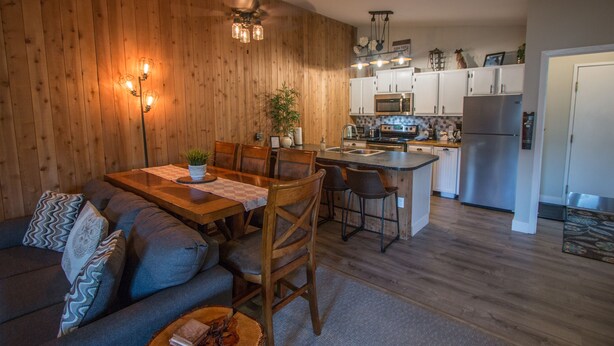 Una cocina moderna con paredes de madera, un comedor con mesa y sillas de madera, y una isla integrada con un lavamanos.