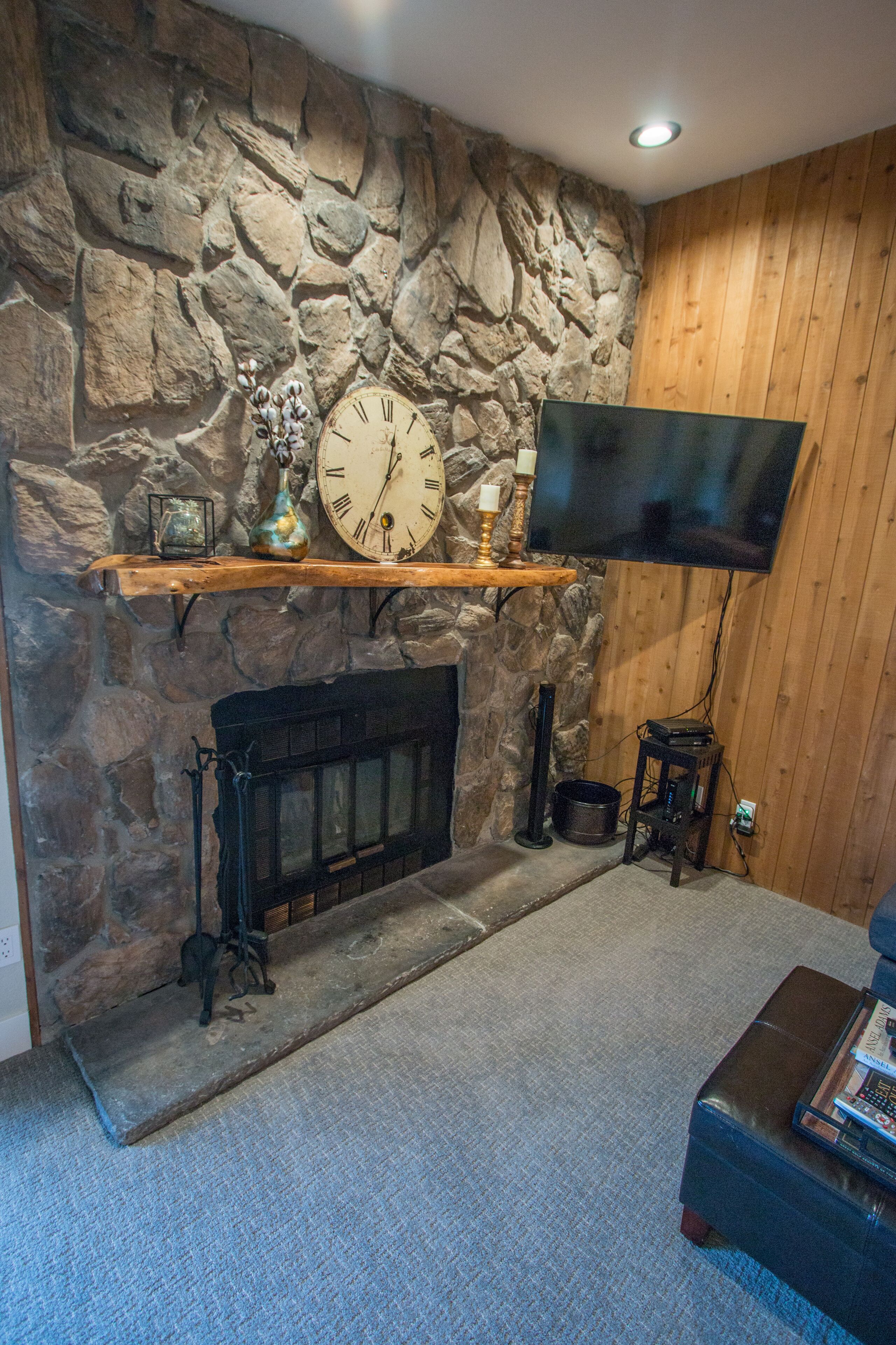 A stone wall with a fireplace, a mounted clock, and a flat-screen TV.