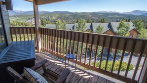 Una terraza de madera con una mesa y sillas, con vista a un paisaje montañoso con casas.