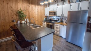 Una cocina con paredes de madera, un refrigerador de acero inoxidable, un microondas y un lavamanos.
