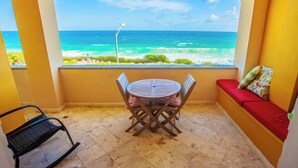 Een balkon met uitzicht op de oceaan, een ronde tafel met stoelen en een rode, gewatteerde bank.